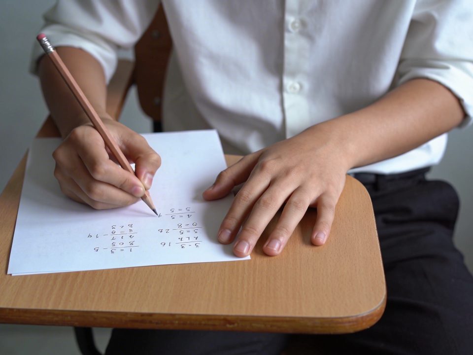 eleve assis a un bureau ecrivant des calculs sur une feuille